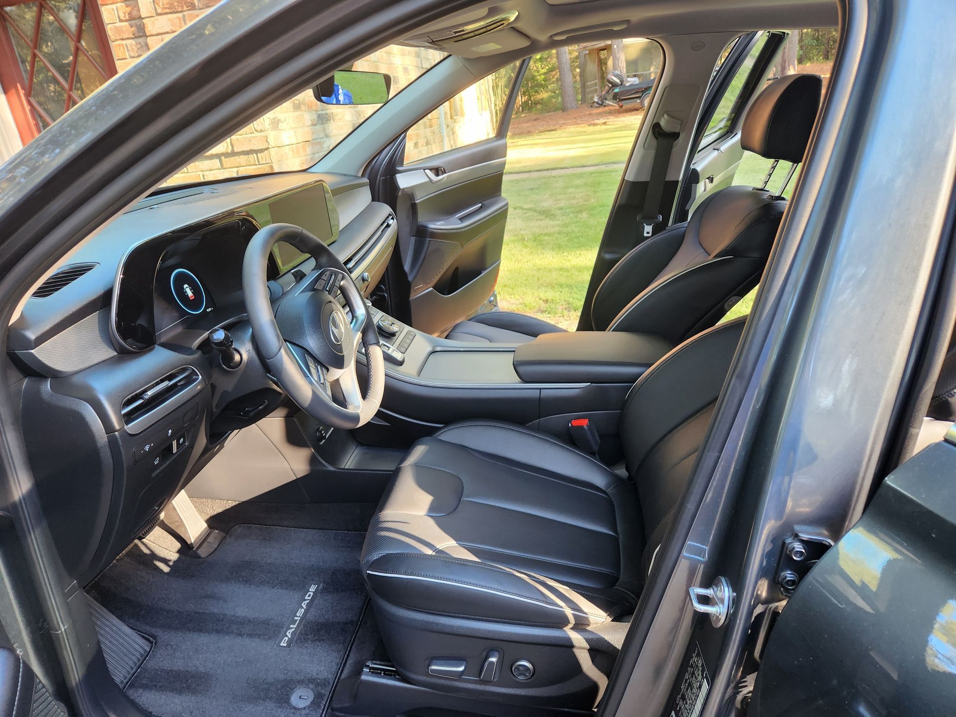 Interior of a dark SUV with black leather seats, dashboard, and open doors, parked outside.