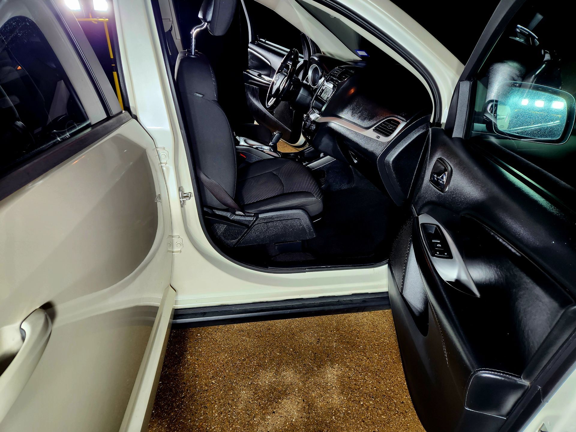 Open door of a white car, revealing black interior and driver's seat.