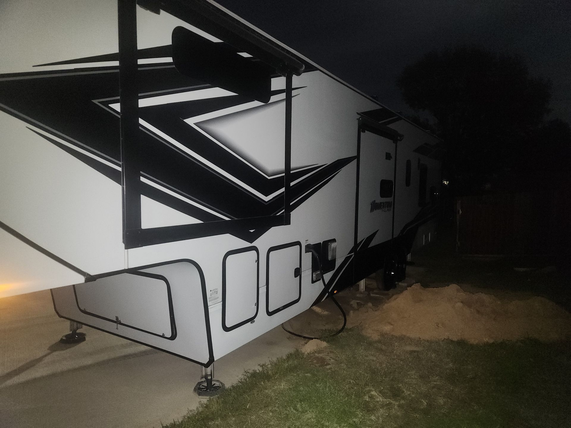A white and black RV at night, parked on a grassy area.