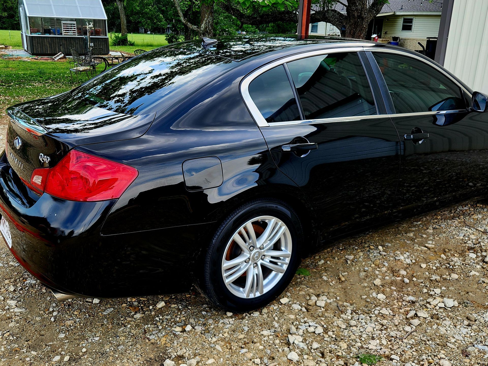 Black Infiniti sedan parked outdoors with tinted windows, a small greenhouse visible in the background.