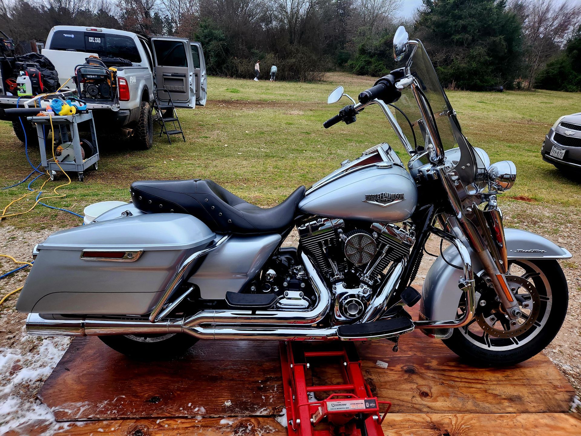 Silver Harley-Davidson motorcycle on a wooden platform, with a red jack. A truck is in the background.