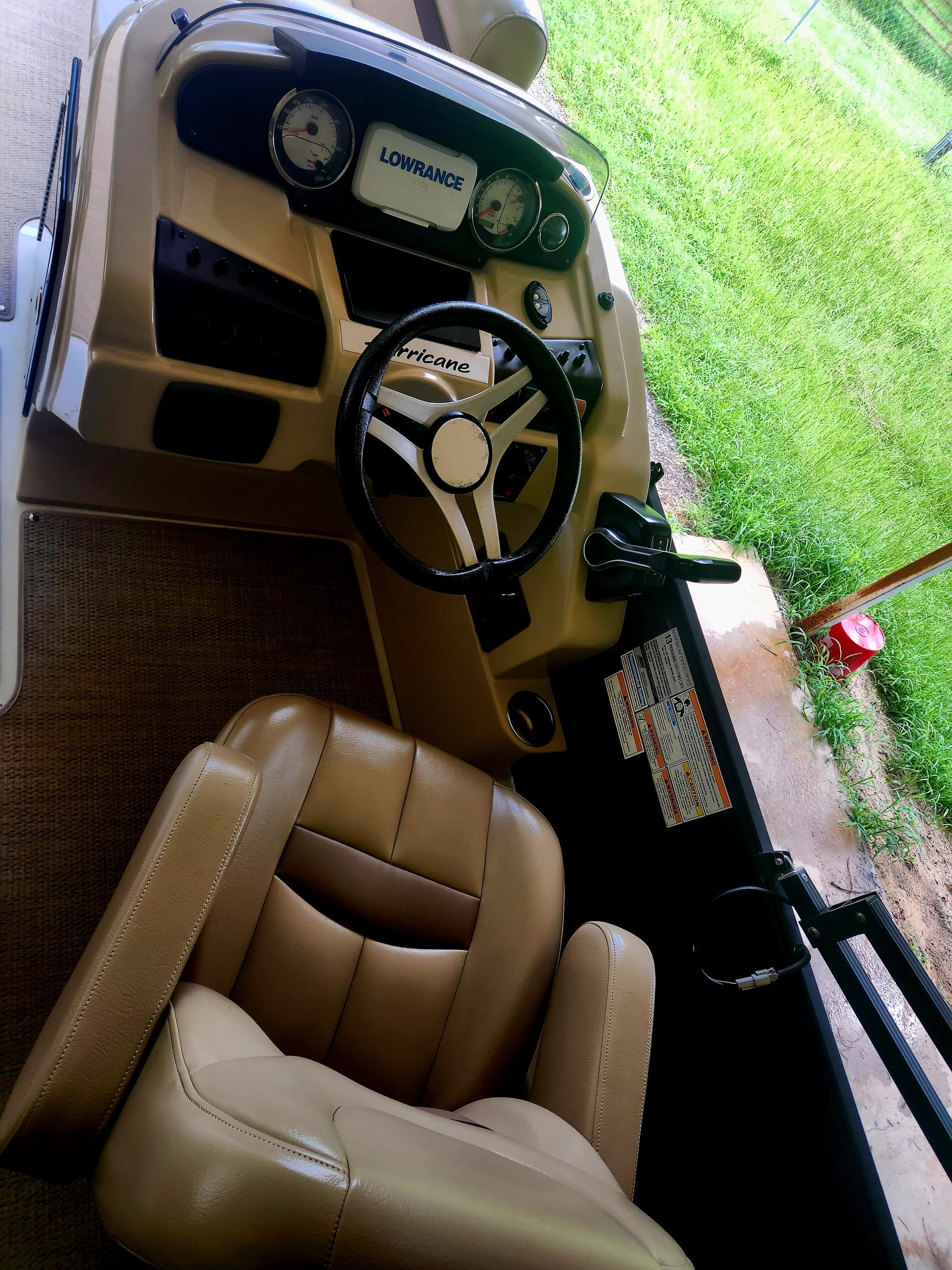 Tan pontoon boat dashboard with steering wheel and captain's chair. Green grass in the background.