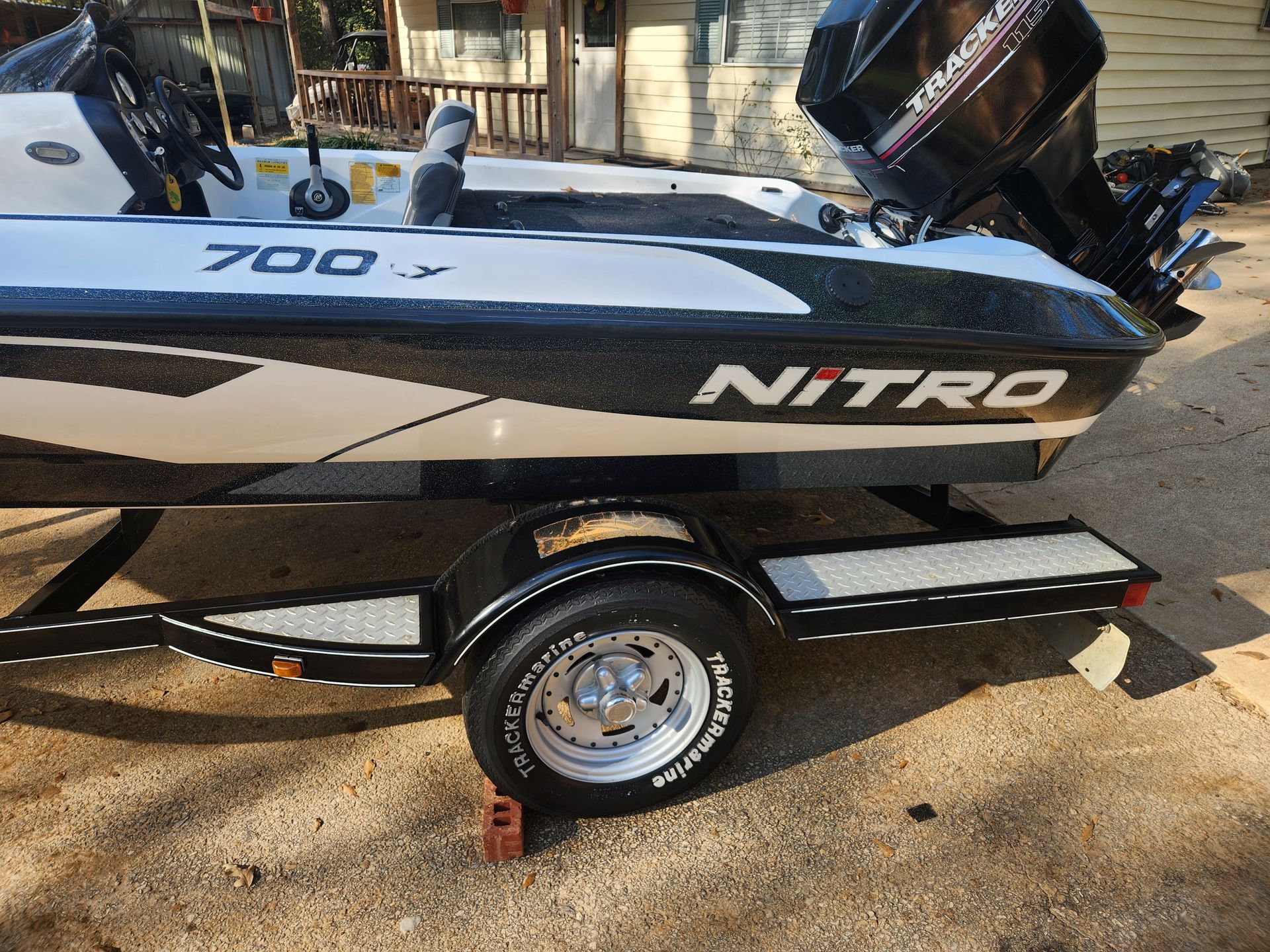 A black and white Nitro boat on a trailer, with a Mercury engine, parked on asphalt.
