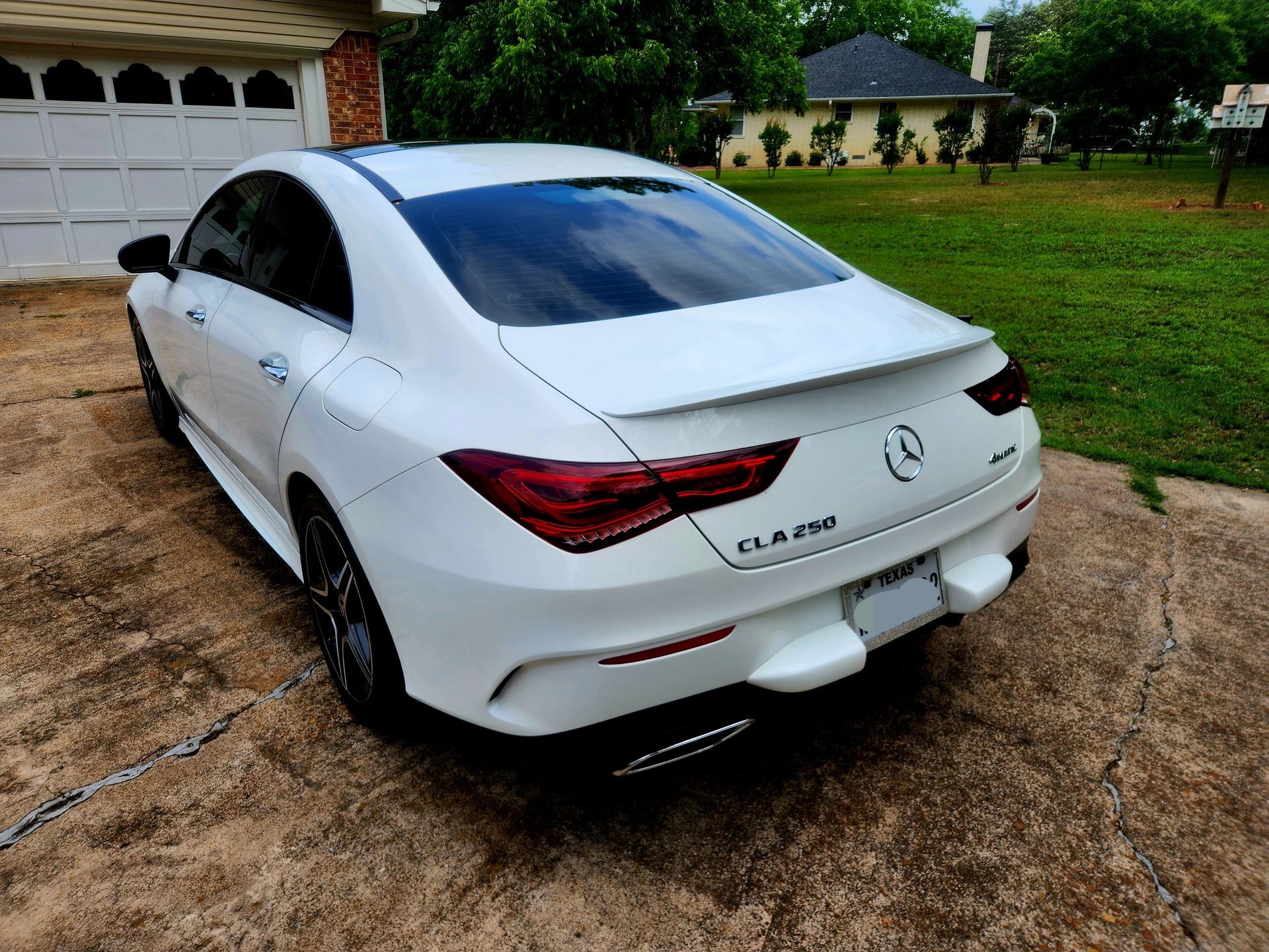 White Mercedes CLA 250 parked on a concrete driveway, in front of a garage.