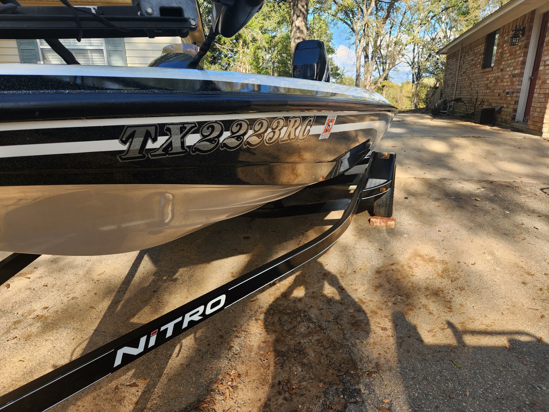 Black and white Nitro TX22 bass boat on a trailer in a driveway, under a sunny sky.