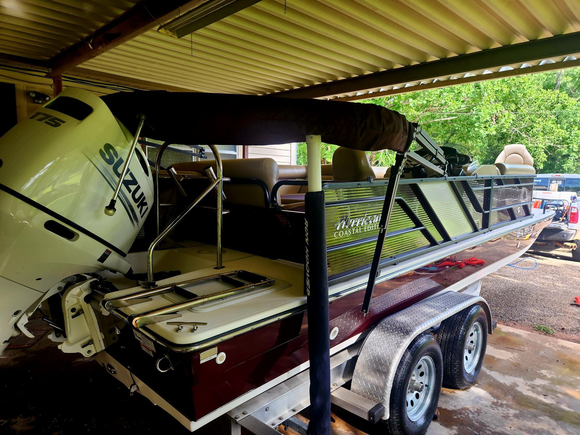 Boat with maroon and white detailing, Suzuki engine, on a trailer under a roof.