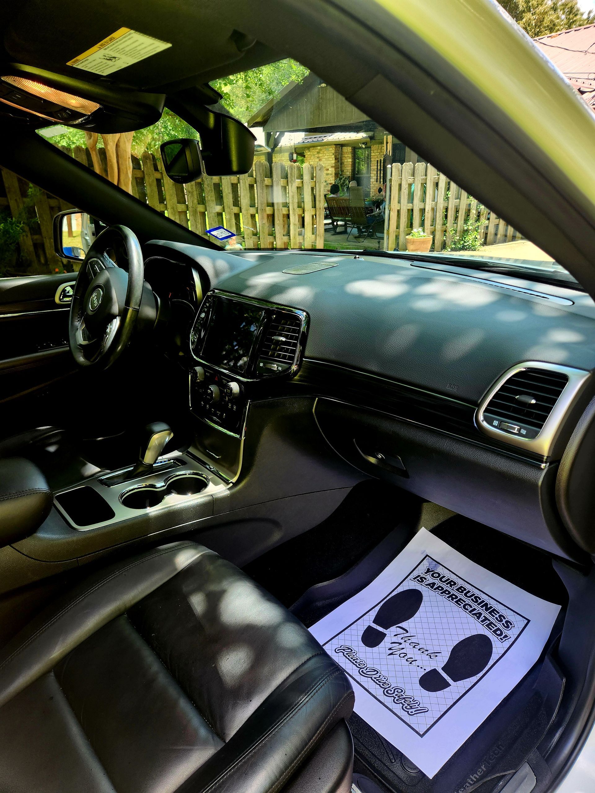Interior view of a black car with a black dashboard, seats, and a foot mat. Sunlight streams in.