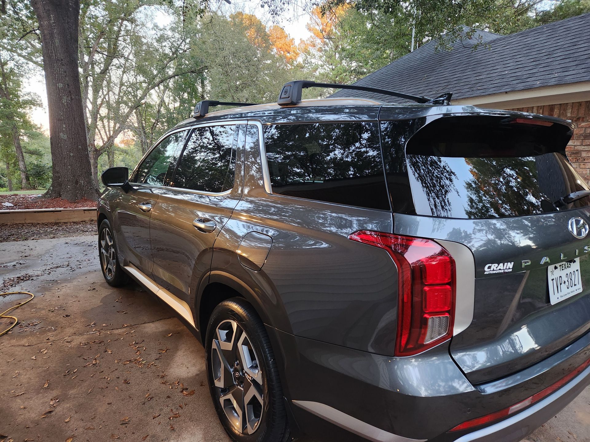 Gray Hyundai Palisade SUV with black roof rack parked outdoors near a brick house.