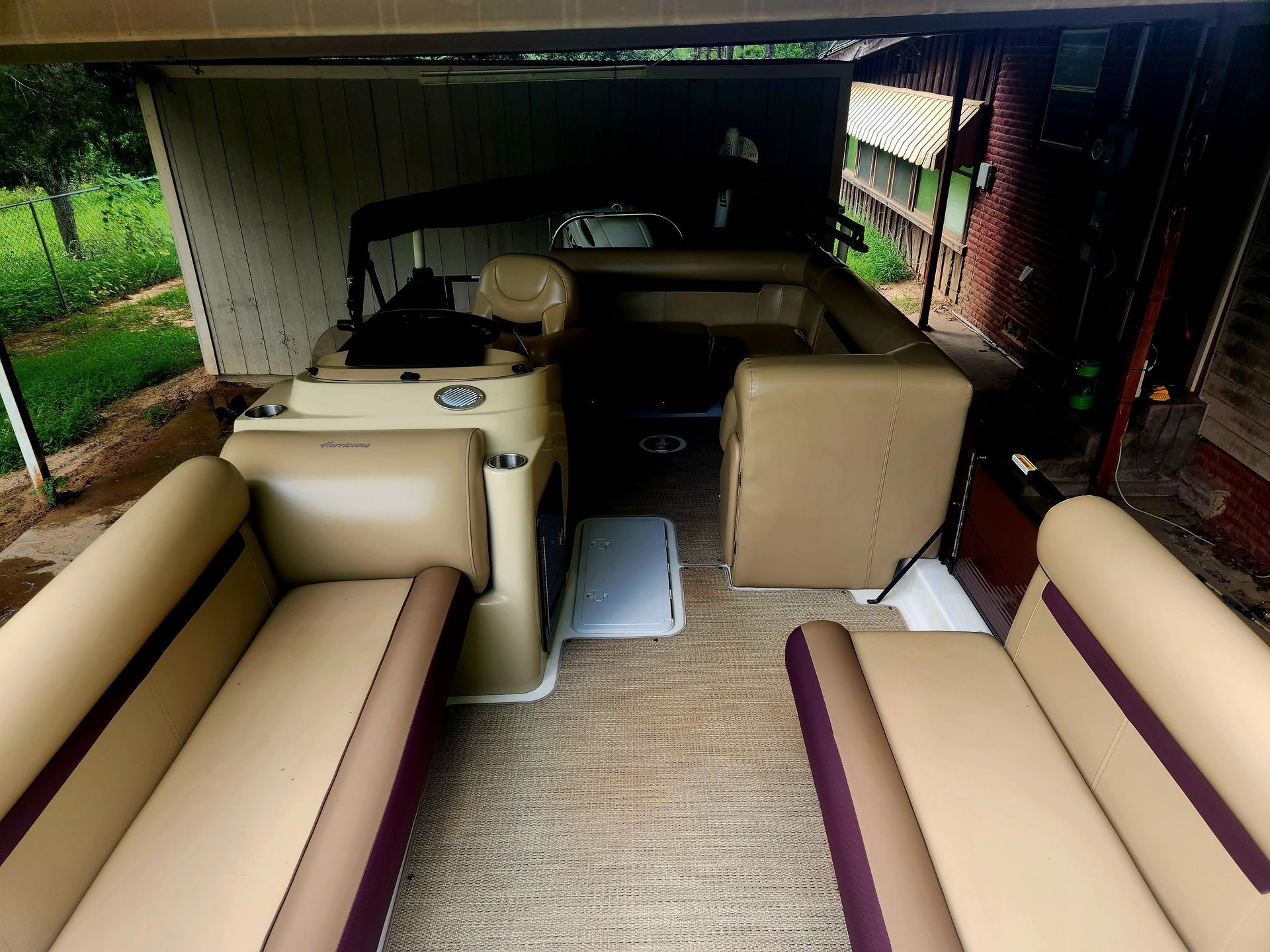Pontoon boat interior with beige and maroon seats, parked under a shelter.