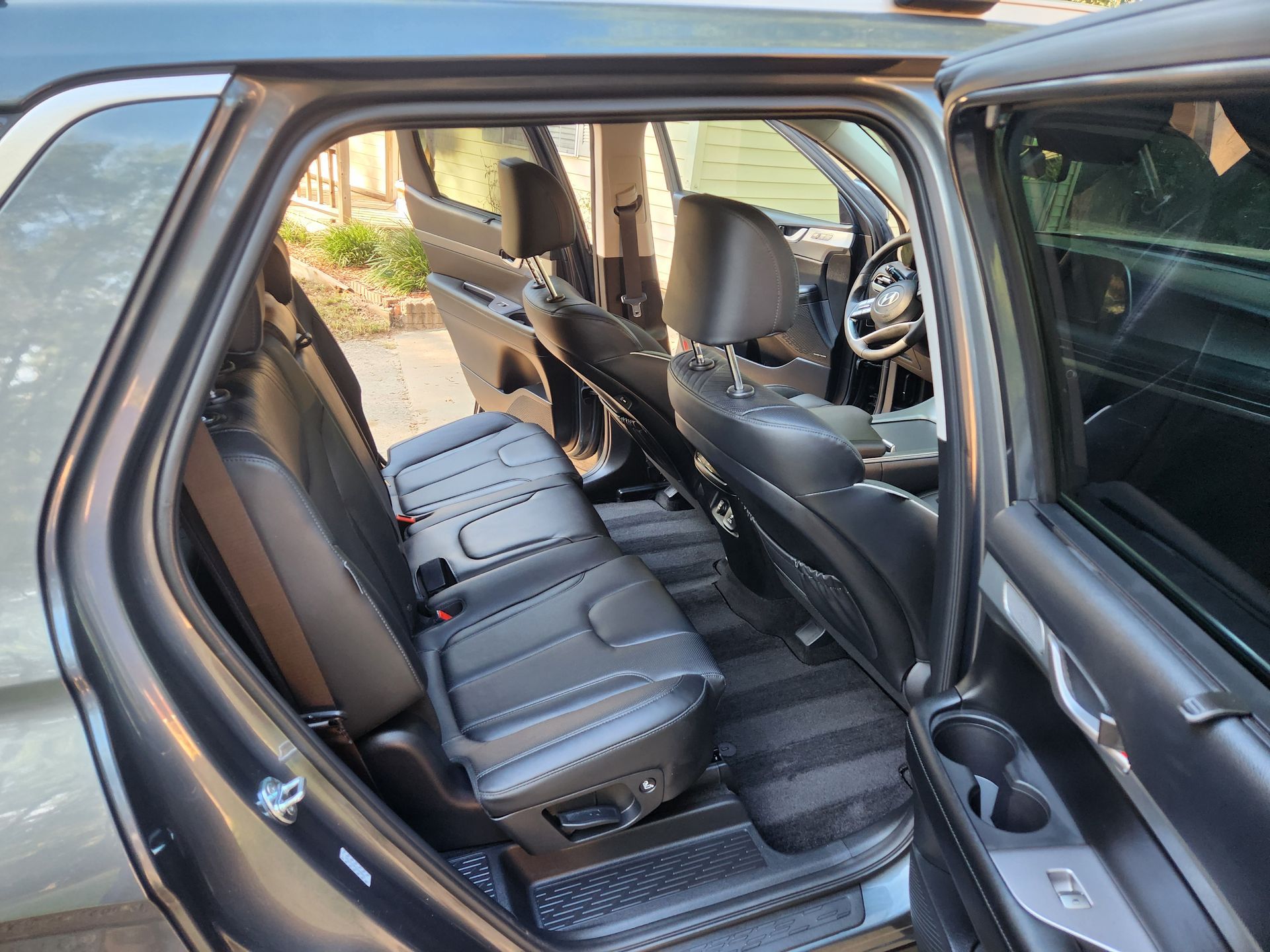 Interior of a dark SUV with open rear door, showing second and third row seats.