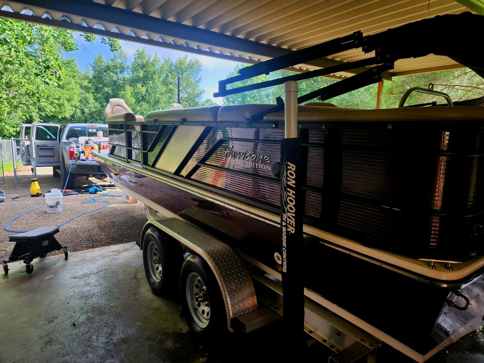 Boat on trailer under a carport; black and brown boat with black lift system.