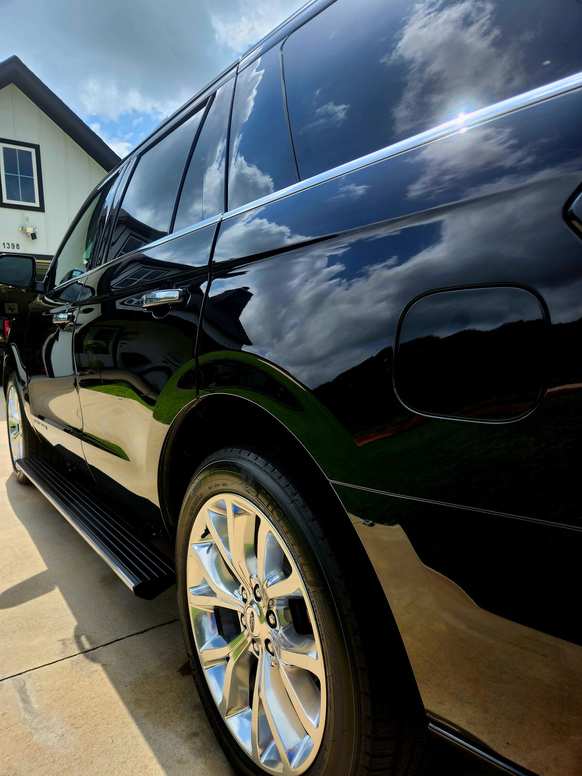 Black SUV with chrome wheels reflecting clouds, parked on a driveway in front of a house.