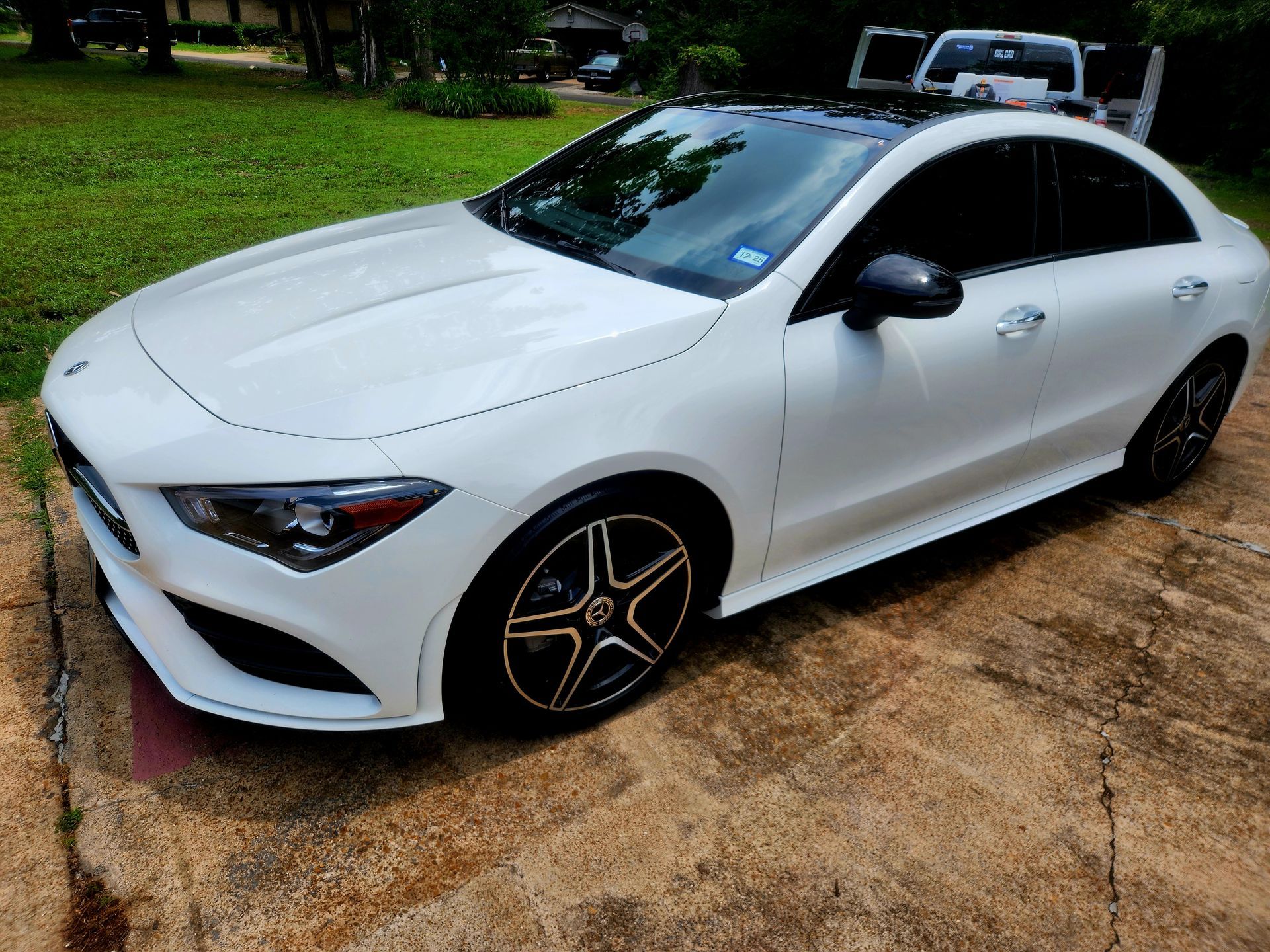 White Mercedes CLA sedan parked on a driveway with a black roof and tinted windows.