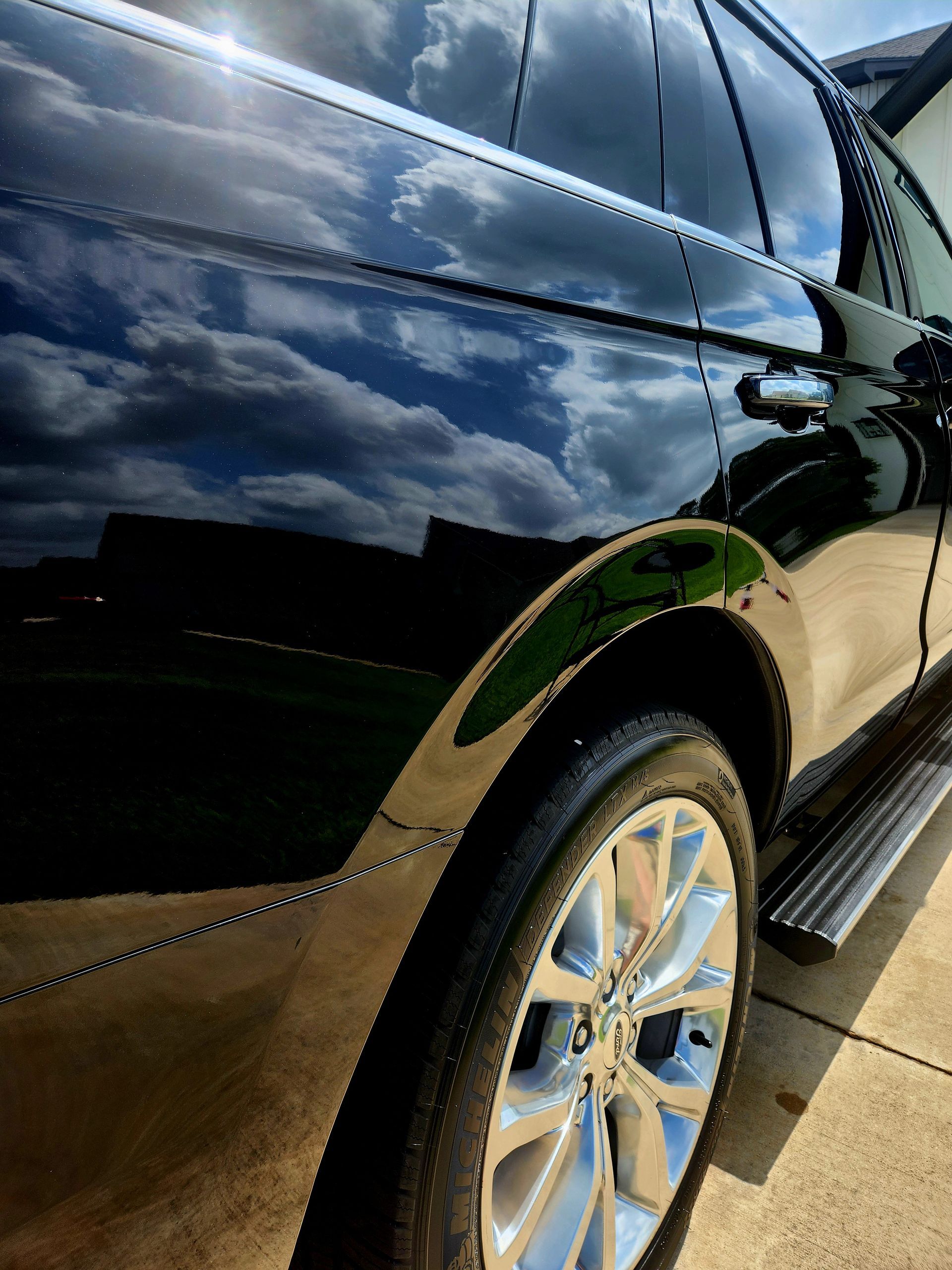 Black SUV with shiny paint reflecting clouds, a wheel, and a running board.