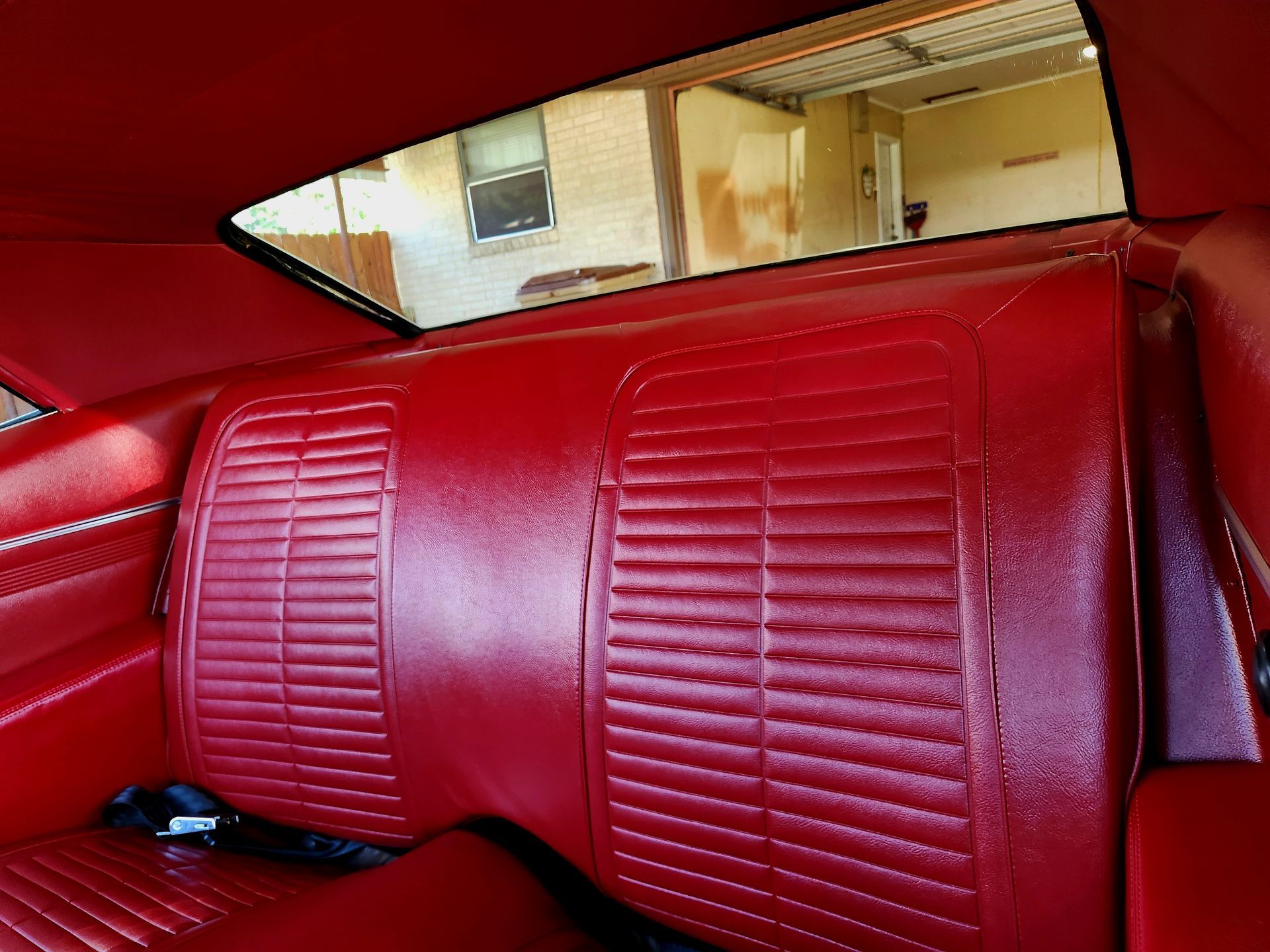 Red interior car seat with ribbed design; view through the back window of an outdoor garage.