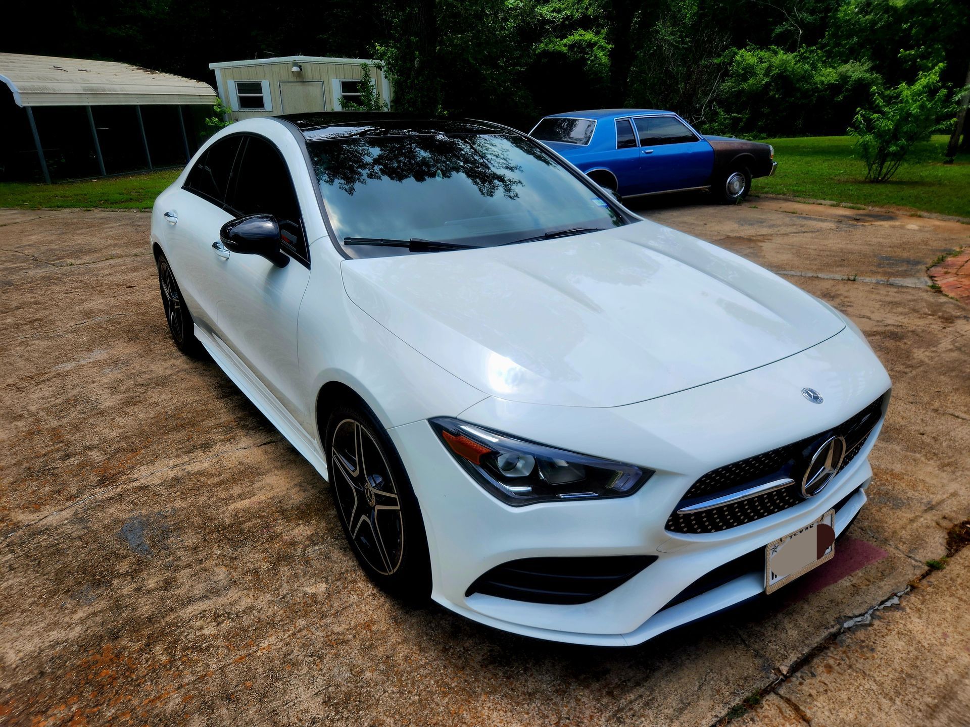 White Mercedes-Benz car with black roof parked on a concrete driveway; a blue car is visible in the background.