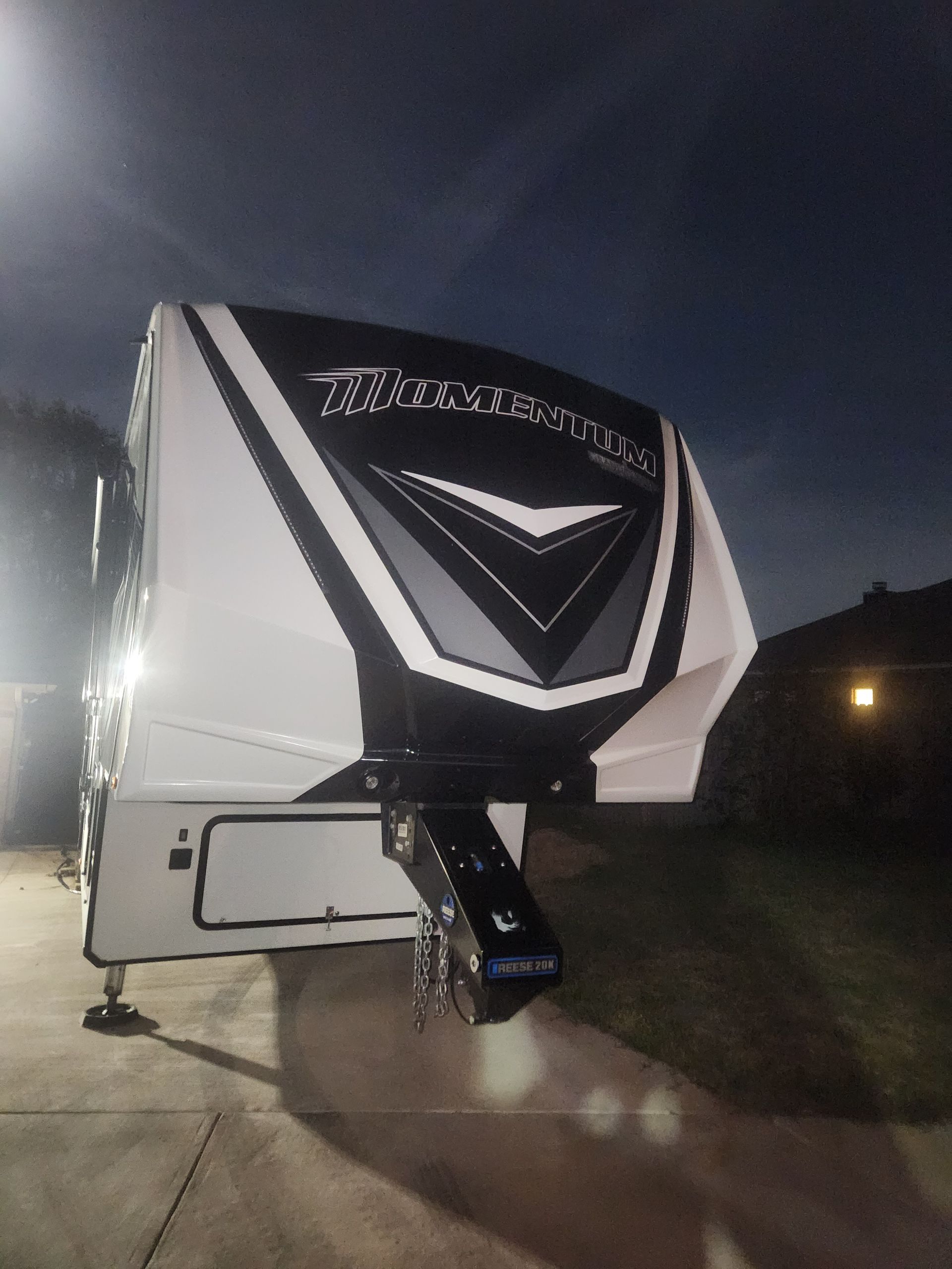 White and black fifth wheel RV with black hitch, parked at night.