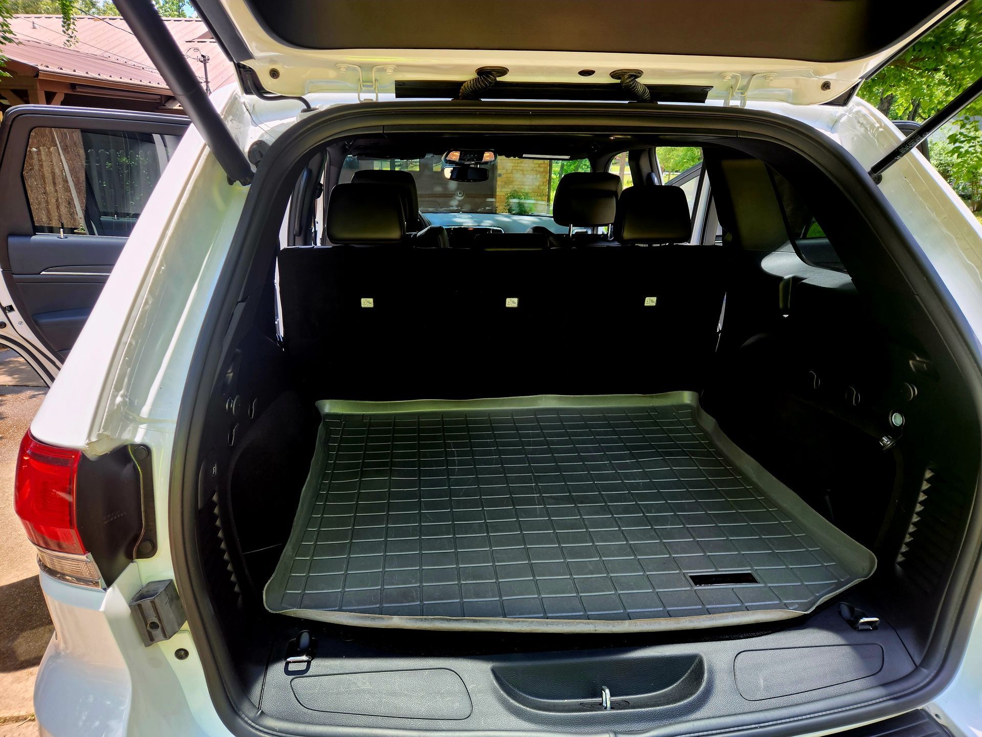 Open white SUV trunk with a black mat and backseats.
