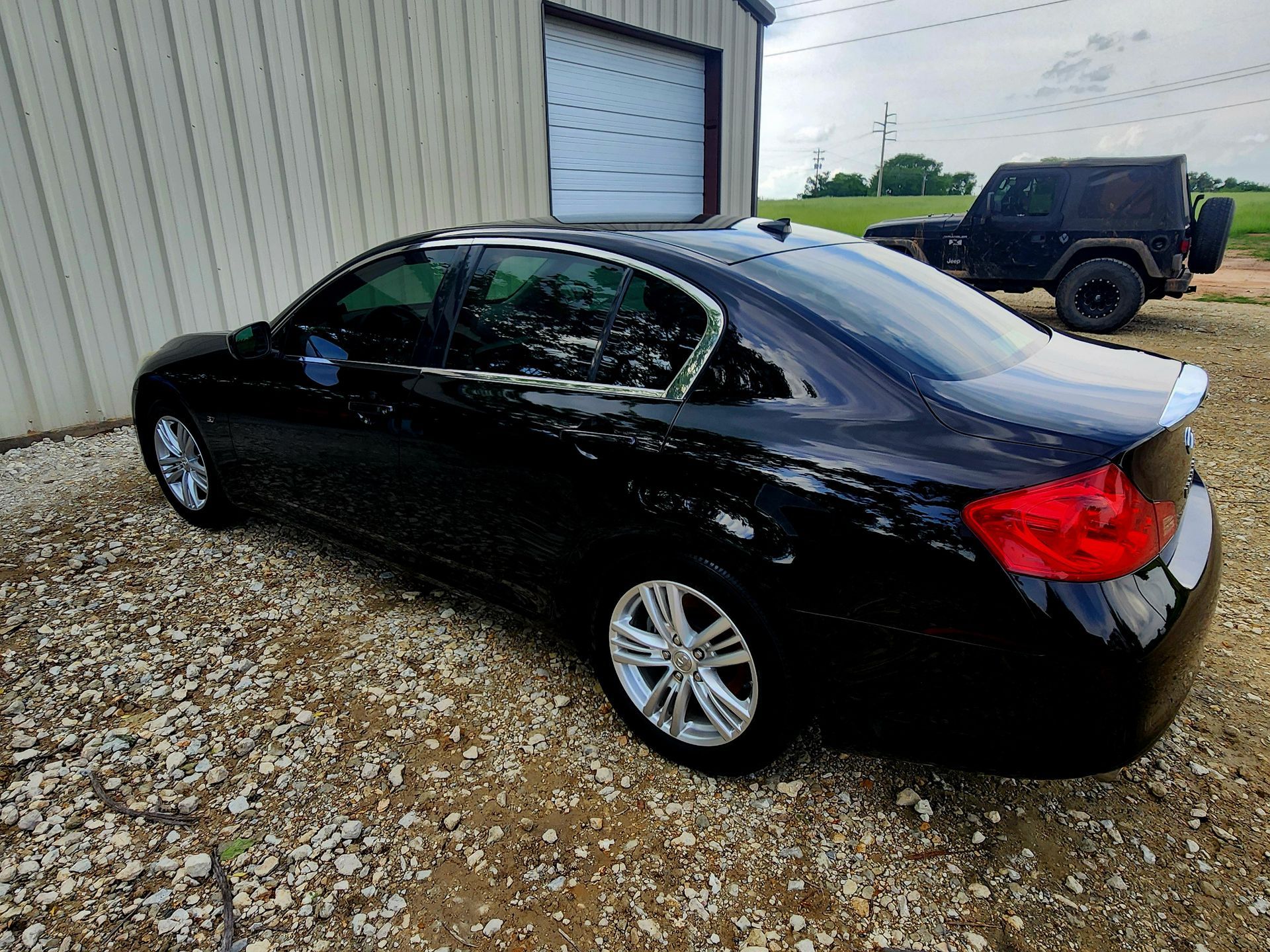 Black sedan parked outside a building with a jeep in the background on a gravel lot.