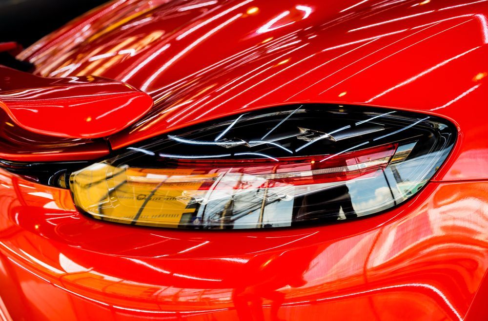 Close-up of a shiny red sports car with an illuminated headlight.