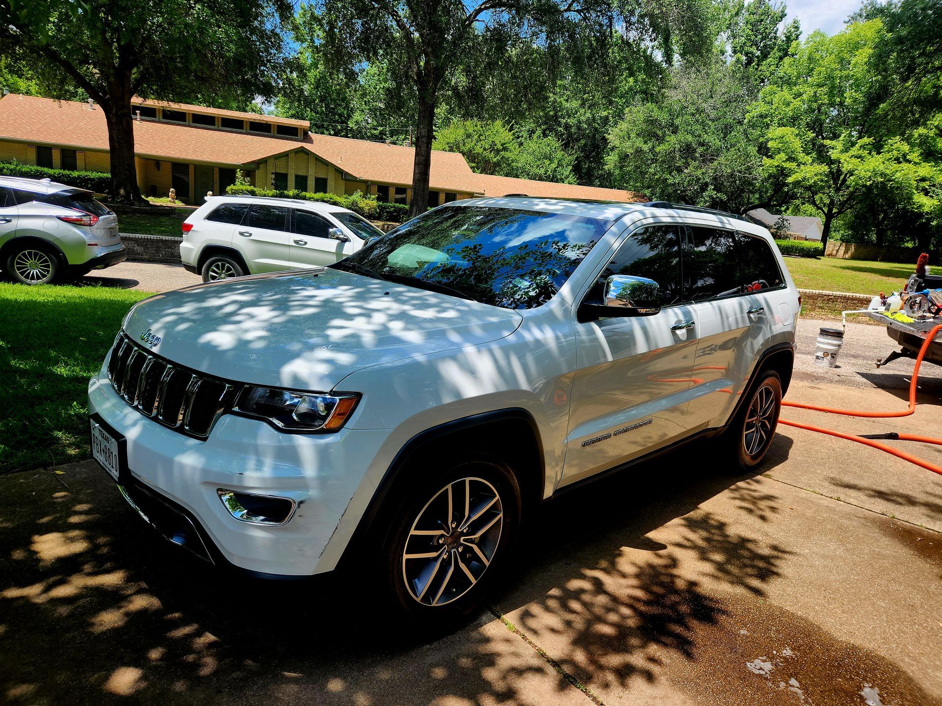 White Jeep Grand Cherokee parked on a driveway, sunny day. Another Jeep is in the background.