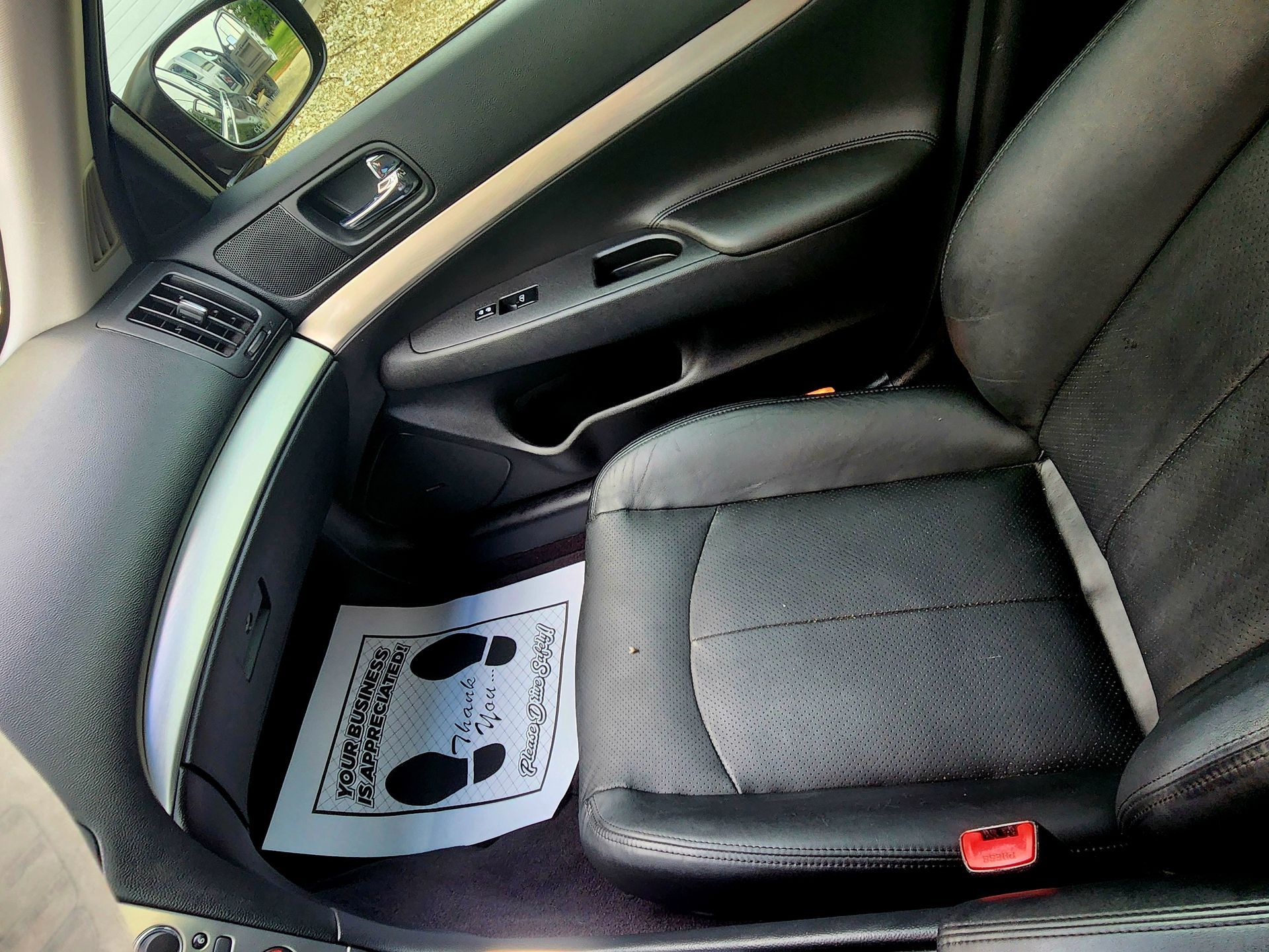 Black car interior with a black leather seat, a foot mat, and the door panel.