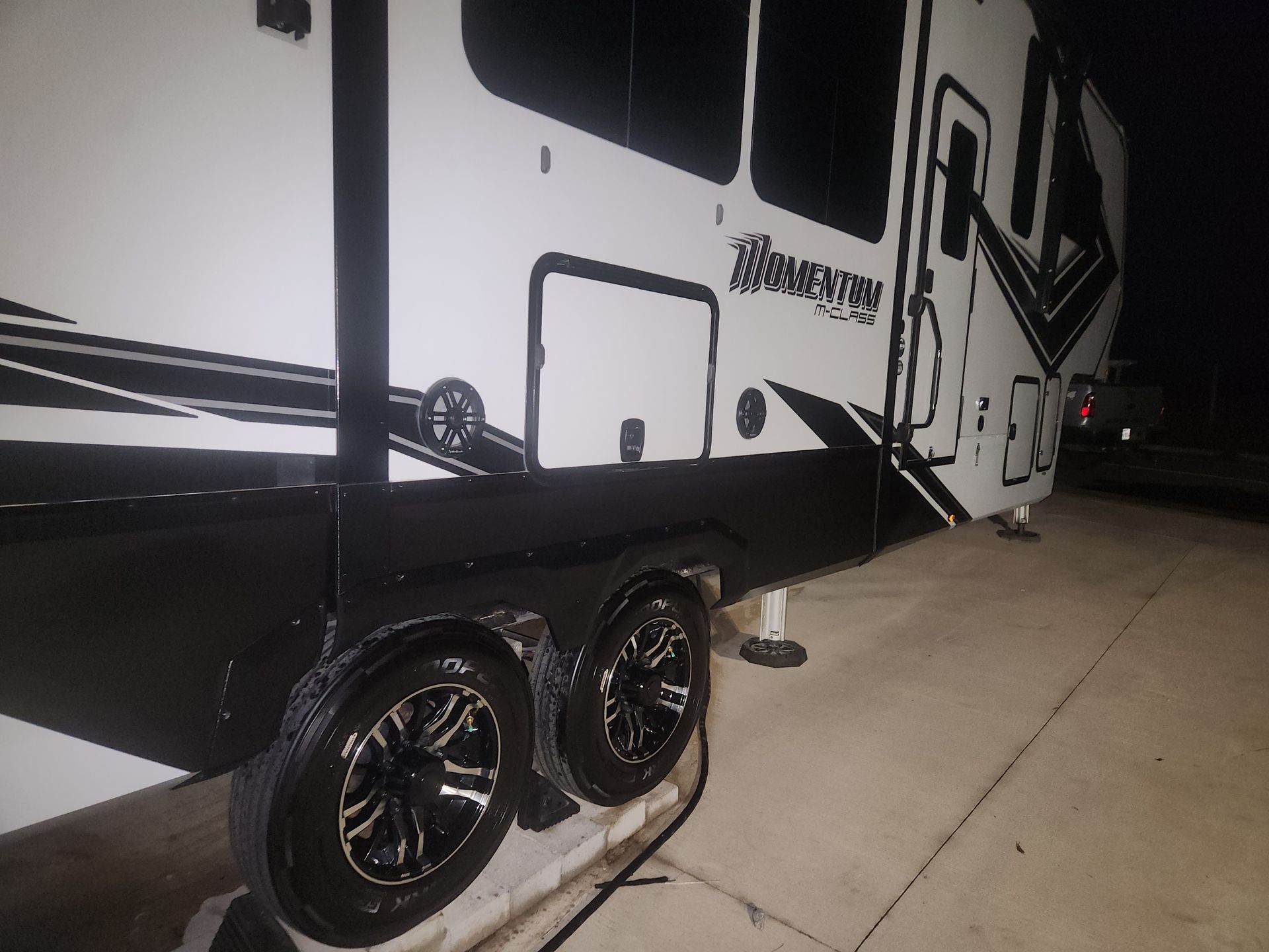 Black and white RV parked on a concrete surface at night, with two visible tires.