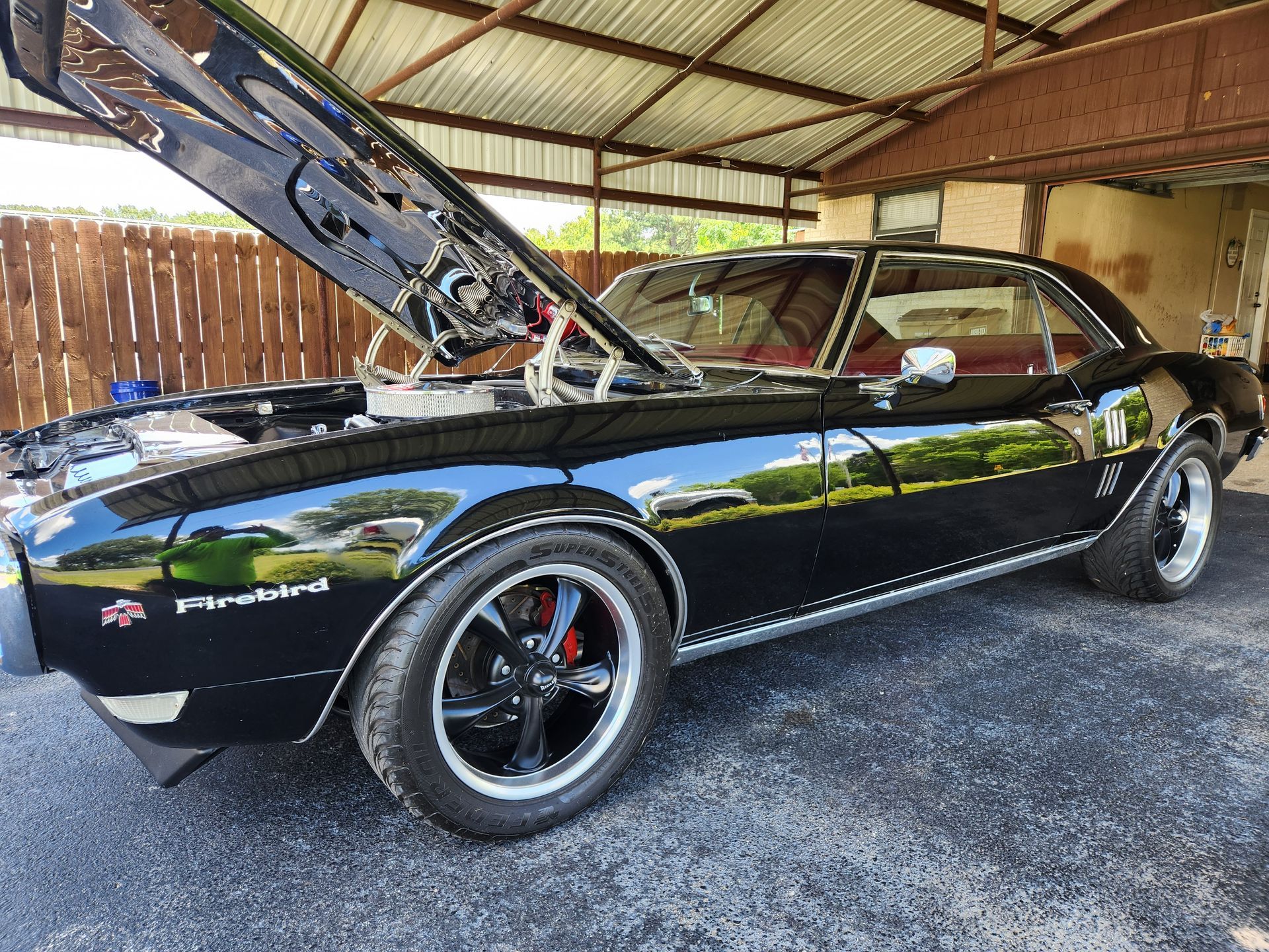 Black classic Pontiac Firebird with hood open, parked under a shelter.