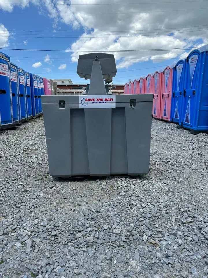 A row of portable toilets are lined up in a gravel lot.