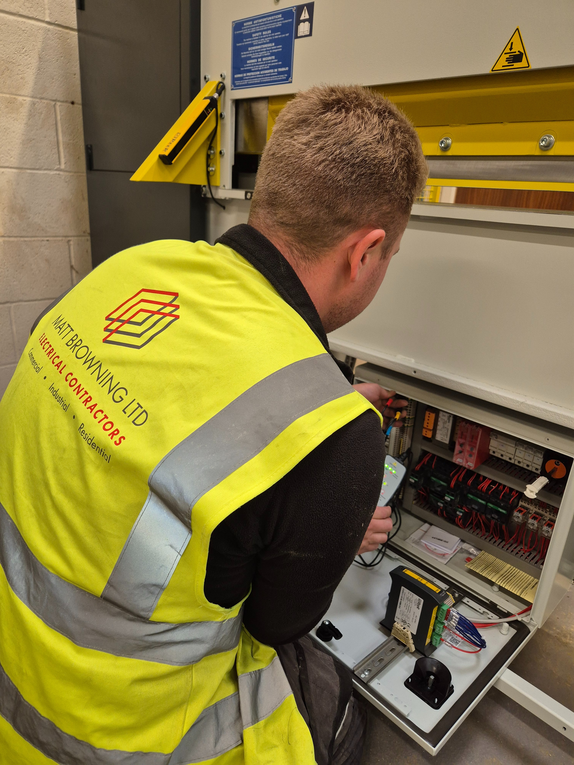 A qualified electrician from Matt Browning Electrical carrying out phase rotation tests at the control panel of a newly installed joinery machine at a manufacturing workshop in Oxfordshire. The Casati guillotine supplied by Scott + Sergeant is connected to a 3-phase electrical supply ready for commissioning.