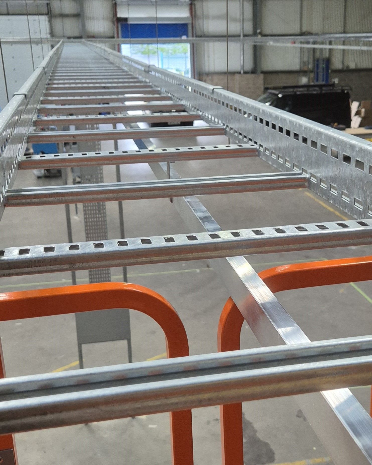 A view along galvanised steel cable ladder being installed at high level in a factory warehouse in Berkshire by Matt Browning Electrical. The cable ladder provides cable support for electrical distribution cables to supply 3-phase power to machines and distribution boards.