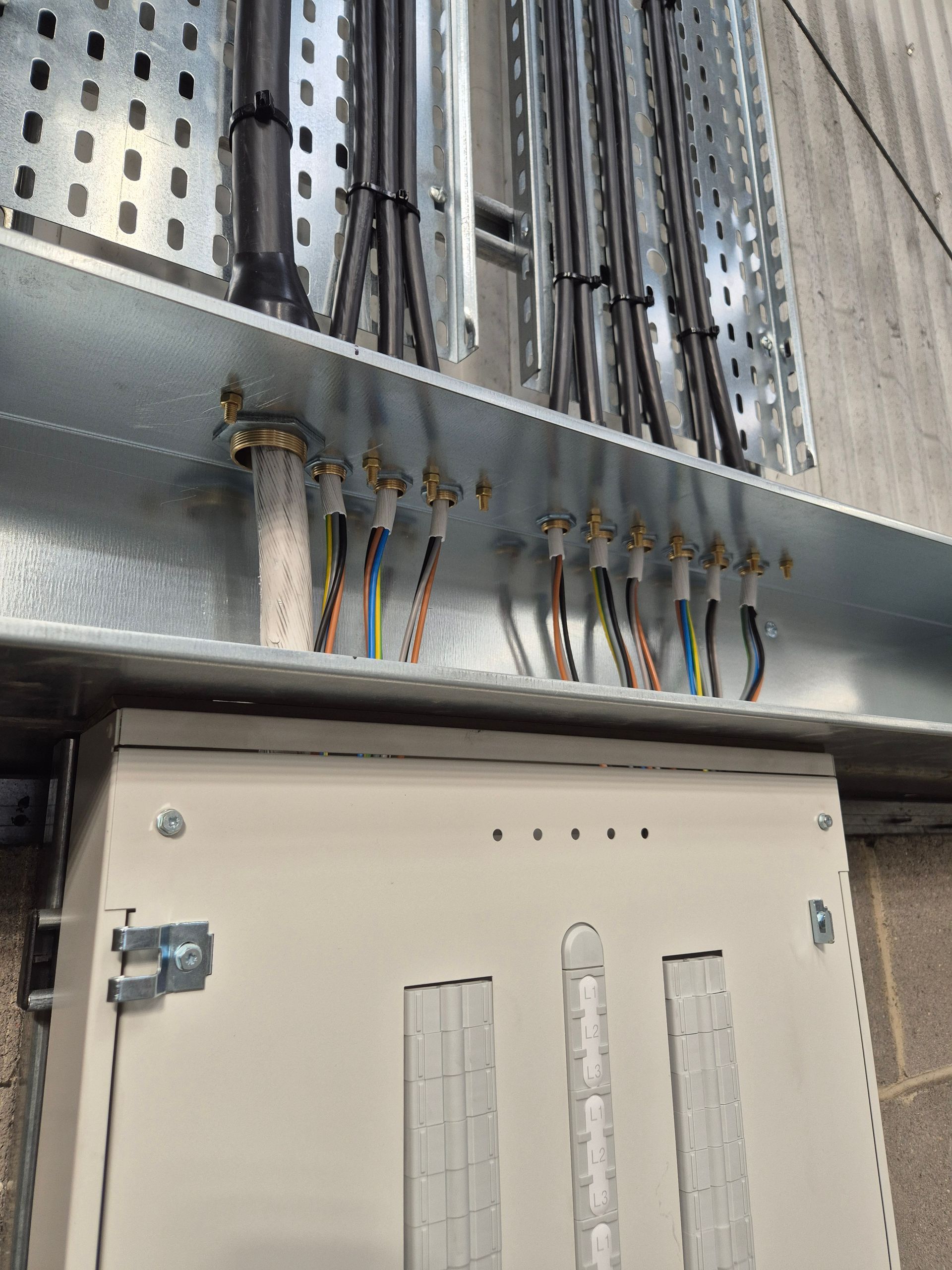 SWA cables on steel cable tray neatly glanded and terminated into galvanised steel cable trunking containment above a Hager 3-phase 125A electrical distribution board at a Warehouse electrical fit out project in Berkshire – installed by the commercial electricians at Matt Browning Electrical who are based locally in Bracknell. The distribution board will supply production process machines via local isolator switches and machine connections.