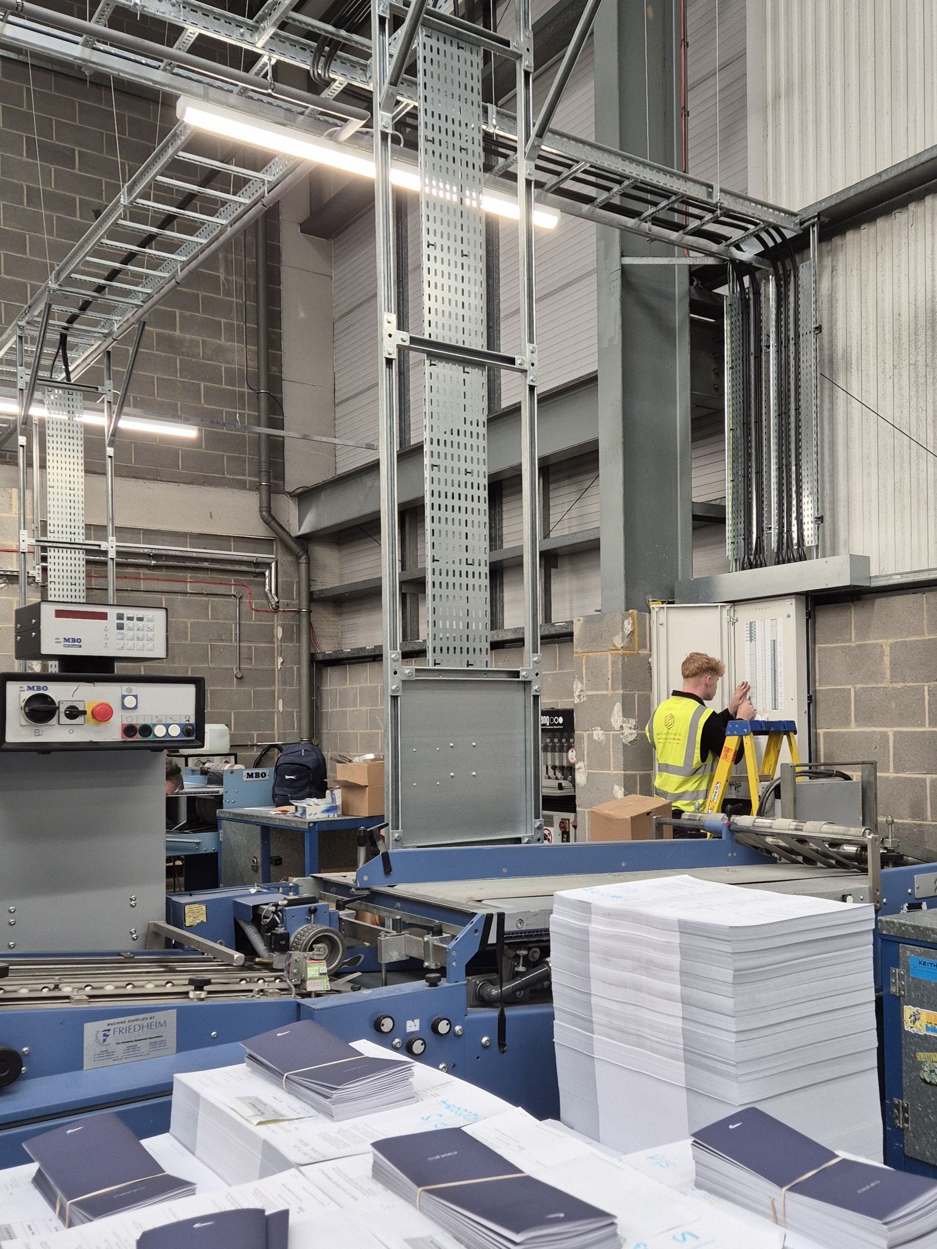 An electrical fit-out project at a manufacturing company in a newly leased commercial premises in Berkshire. The electrician from Matt Browning Electrical is applying final labelling to a local 3-phase distribution board that supplies machine and small power, with various types of cable containment such as cable ladder, cable tray, and trunking, and industrial LED lighting.