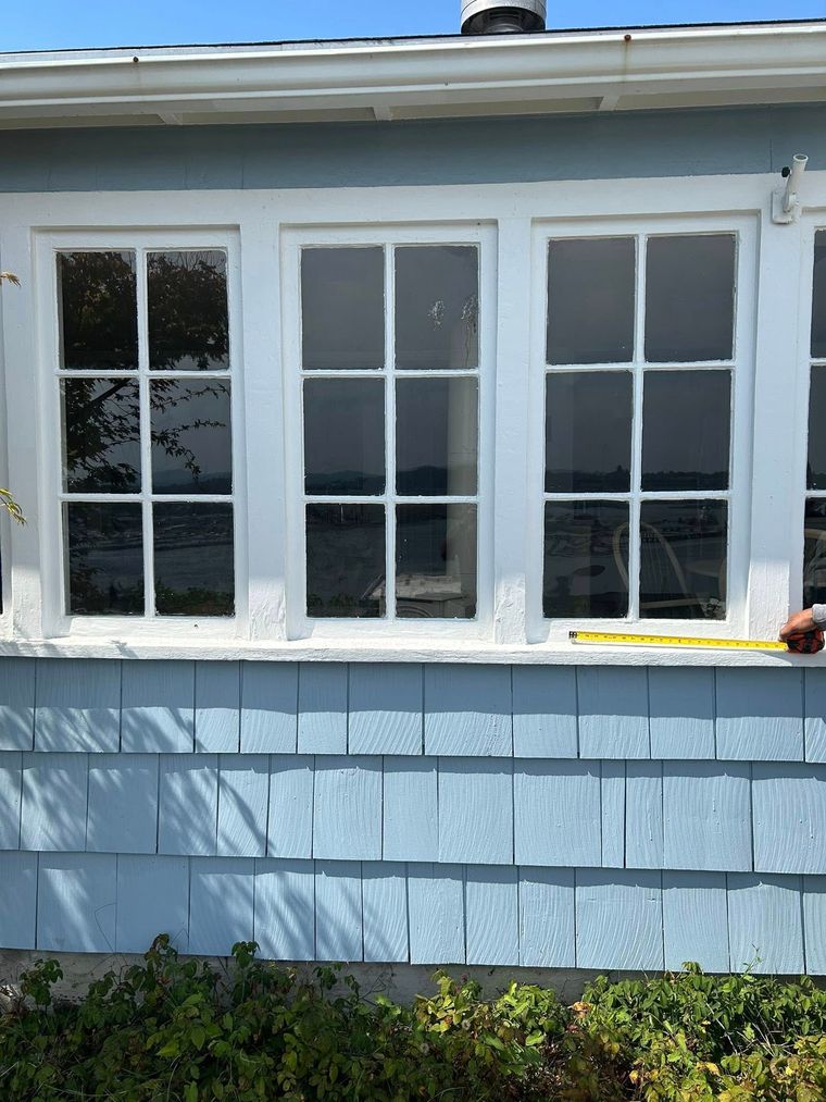 Three white-framed windows overlooking water; blue shingle siding below.