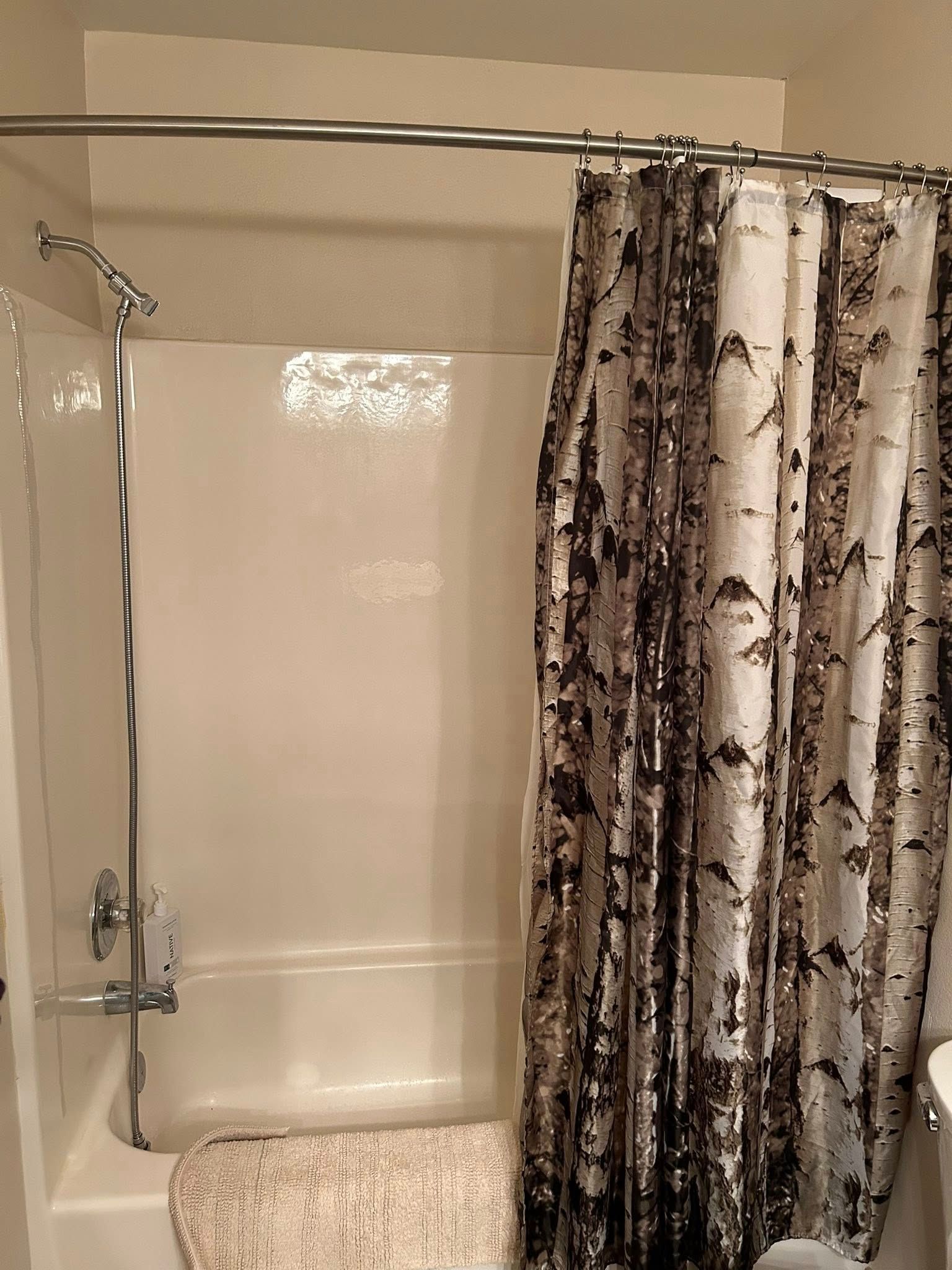 Bathtub with brown and white shower curtain. A tan bath mat sits in front.