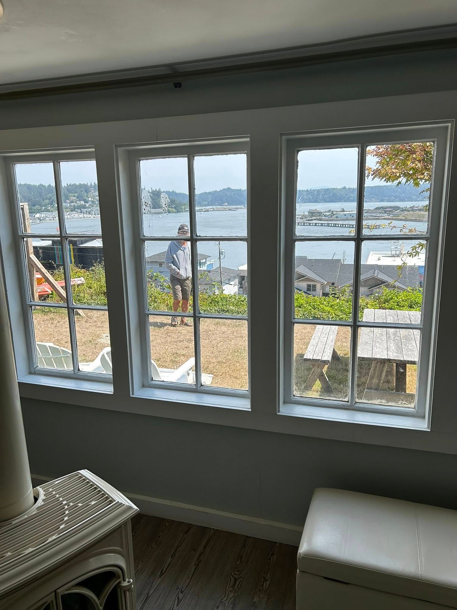 Three white-framed windows overlooking a harbor. A person stands outside, and buildings are visible.