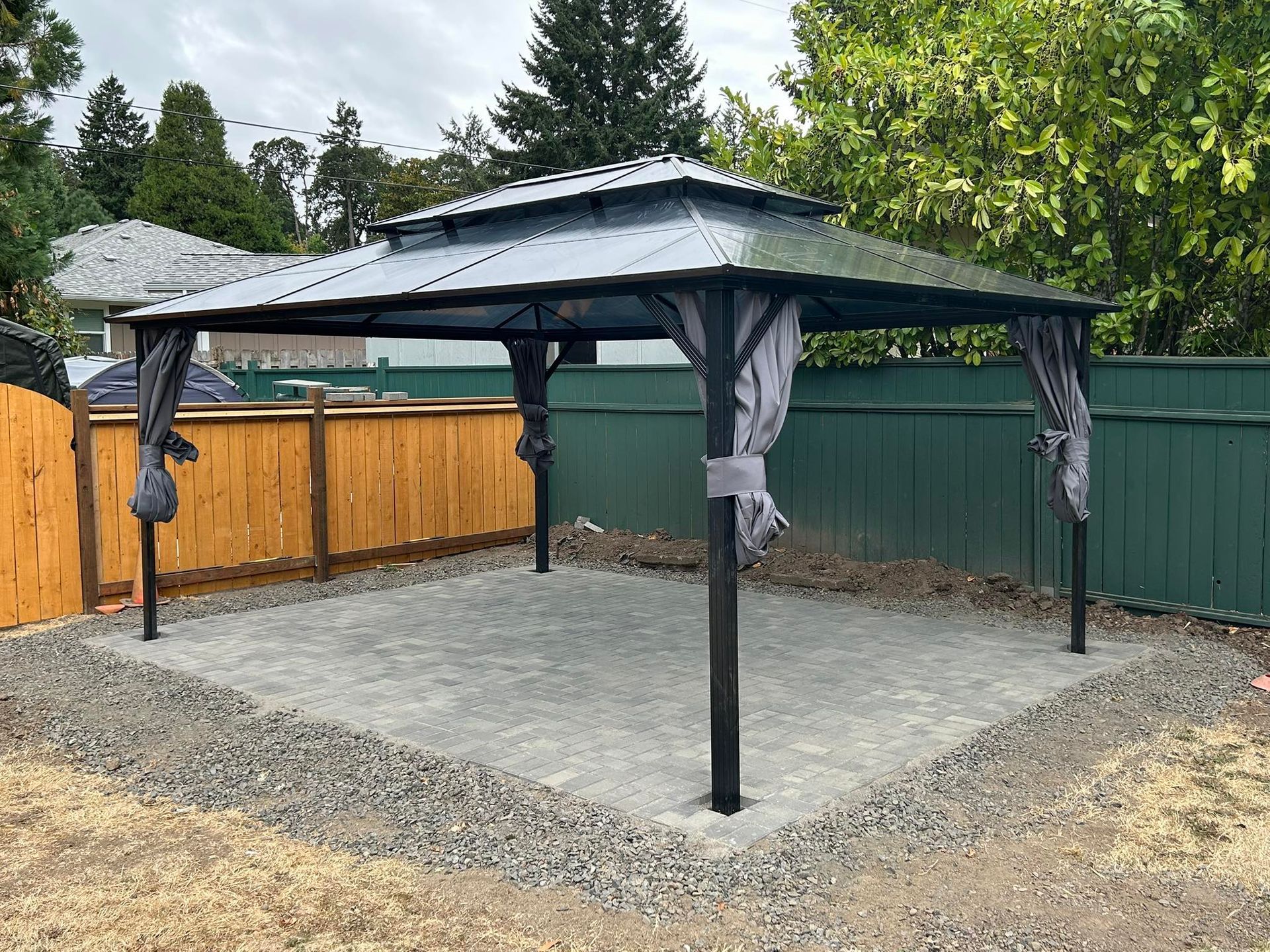 Gazebo on gravel patio, surrounded by fences and greenery.