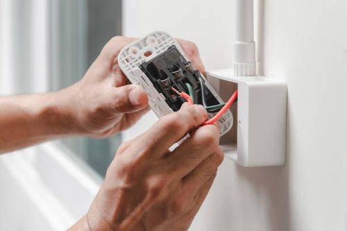 Person wiring an electrical outlet; hands holding wires, white wall and box visible.