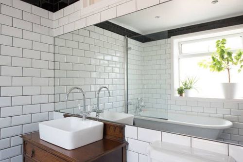 Bathroom with white subway tiles, a large mirror, a bathtub, and a sink on a wooden cabinet.