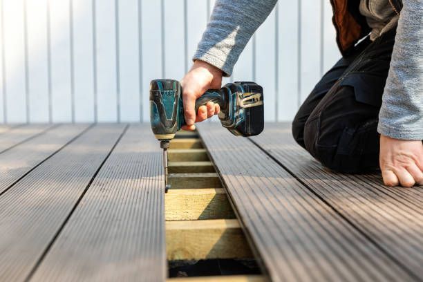 Person kneeling, using a power drill to install deck boards on a wooden frame.