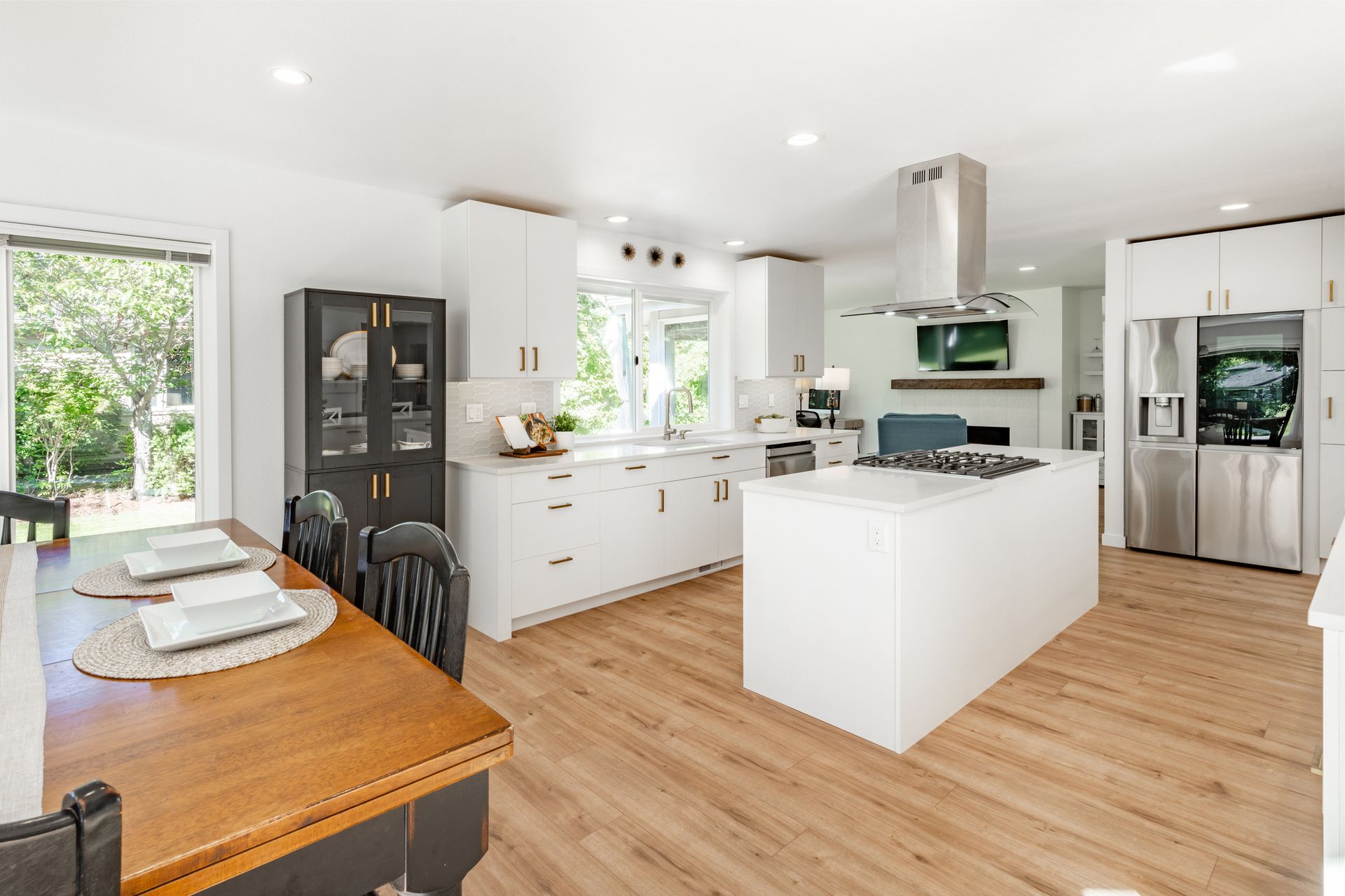 Bright, modern kitchen with white cabinets, an island, and dining table. Sliding door to a backyard.