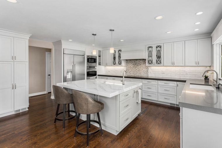 Bright kitchen with white cabinets, island, stainless steel appliances, and dark wood floors.