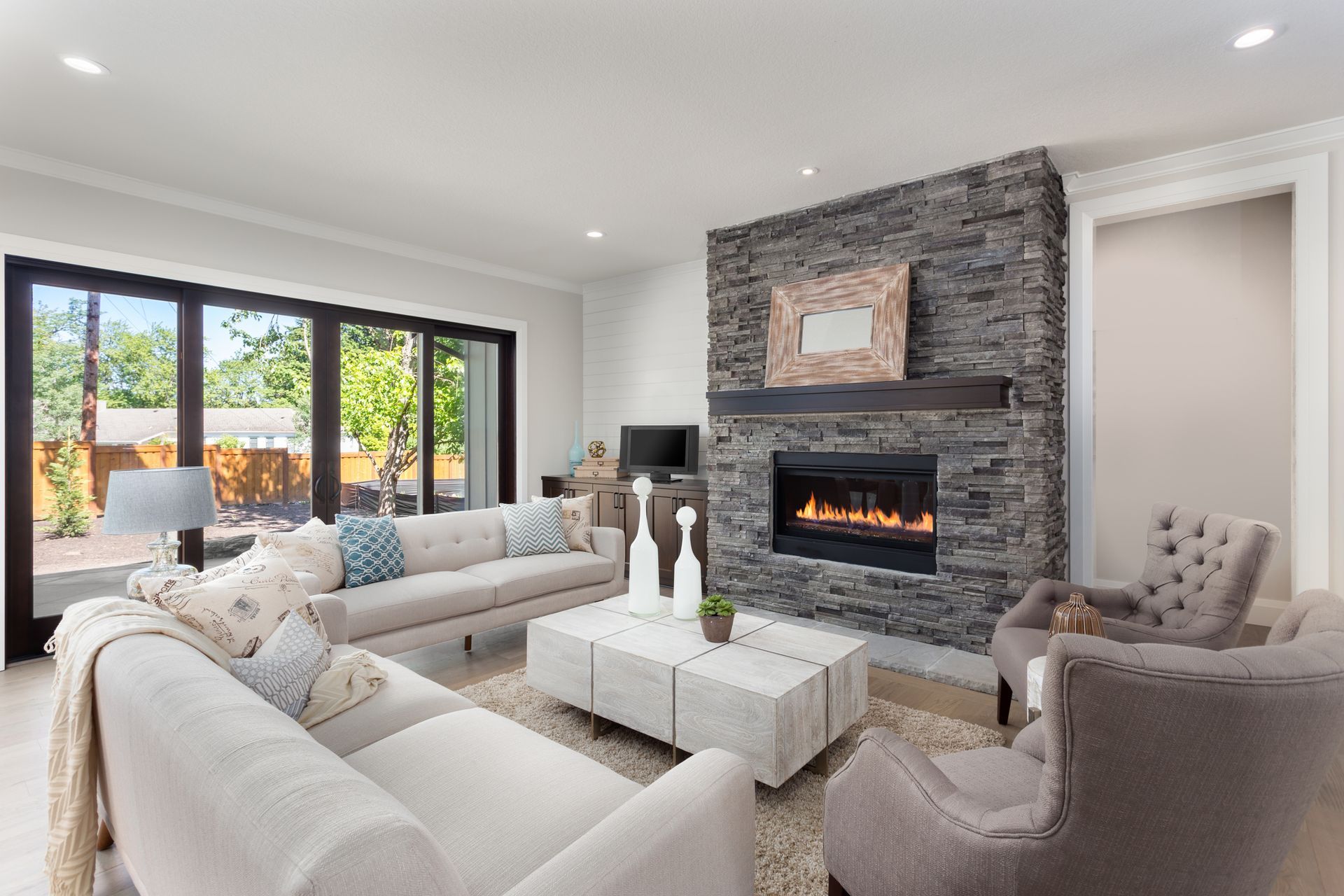 Living room with stone fireplace, couches, and large glass doors leading to the outdoors.