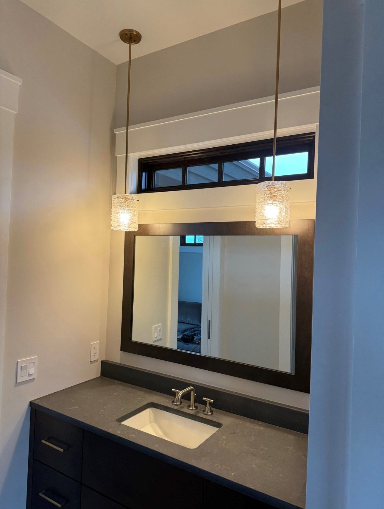 A bathroom with a sink , mirror and lights hanging from the ceiling.