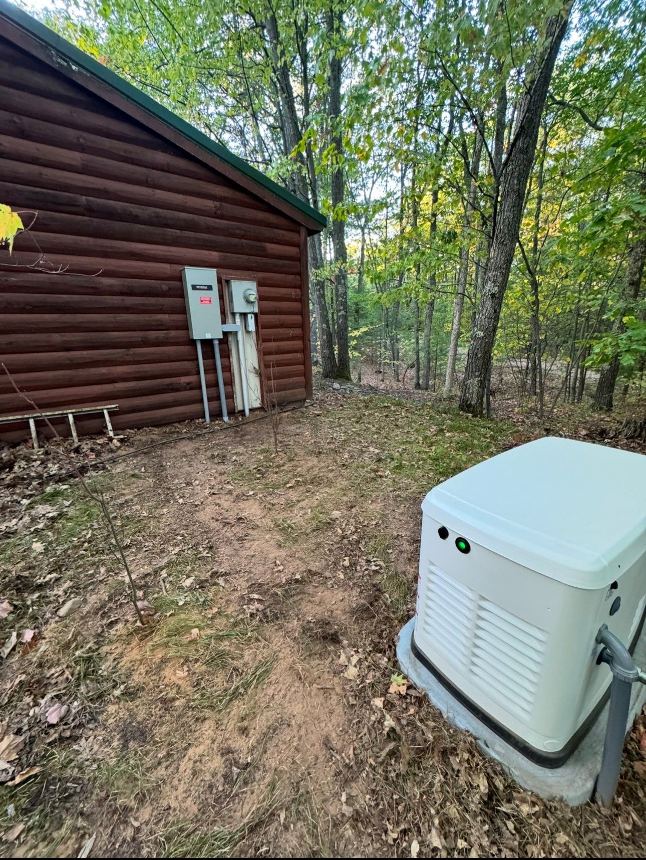 A generator is sitting in front of a log cabin in the woods.