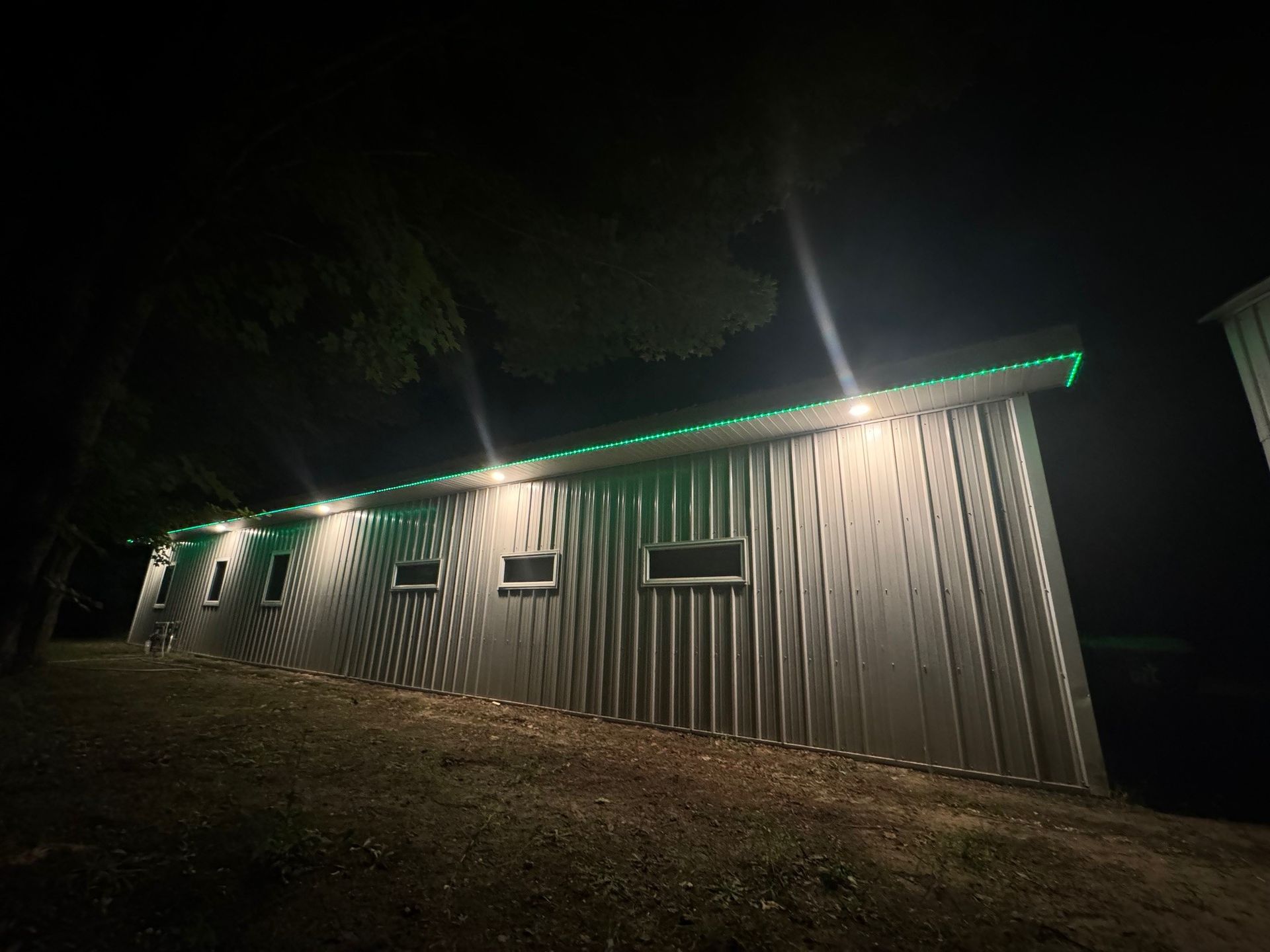 A large metal building is lit up at night with green lights on the roof.