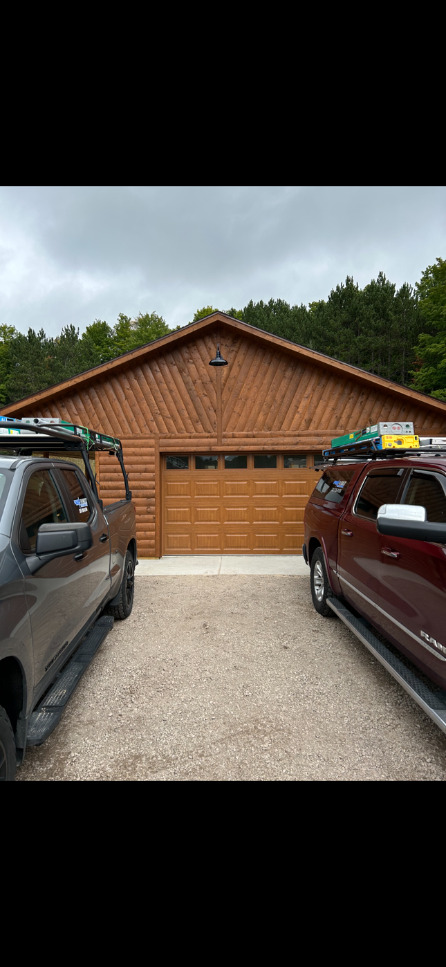 Two trucks are parked in front of a garage with kayaks on top of them.