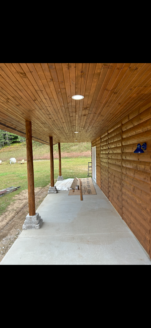 A log cabin with a covered porch and a concrete floor.
