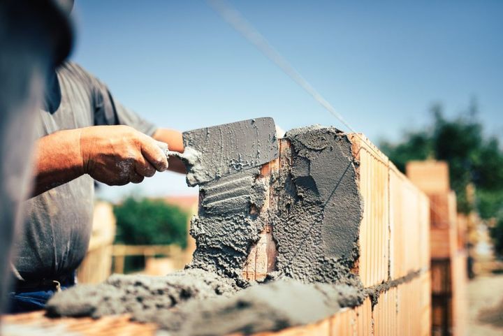Worker troweling wet cement on a brick wall under construction