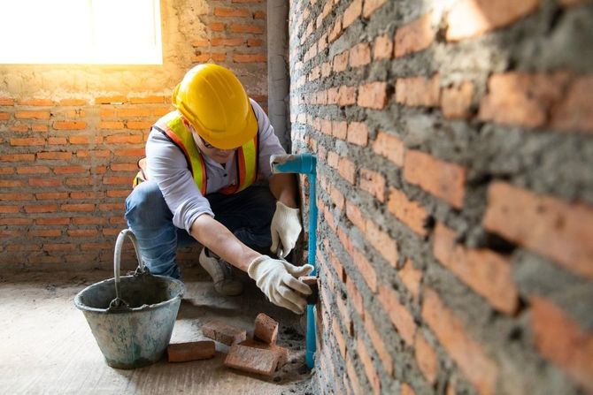 Worker in yellow hard hat applying mortar to a brick wall at a construction site